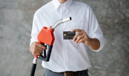 A person stands with a gas pump and a credit card.