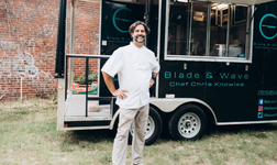 Chef stands smiling in front of food truck