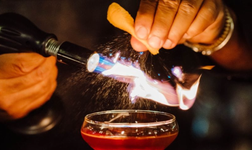 A flame burns an ingredient over a cocktail glass