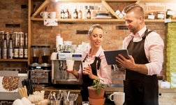 two people working in a restaurant using iPad CRM and making a coffee