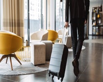Cropped photo of businessman wearing suit walking with suitcase in hotel lobby