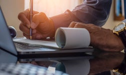 Business man hand sign cheque book with laptop computer on the desk