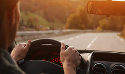 Man at wheel of a car driving with road in the background