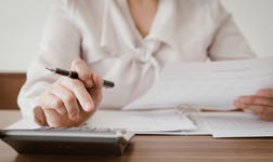 Woman with calculator, pen and pay slips calculating taxes