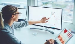 Business woman looking at data charts on a desktop computer and laptop.