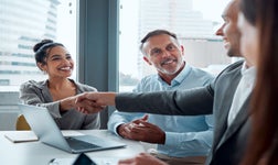Woman smiling and shaking hands as colleague looks on.