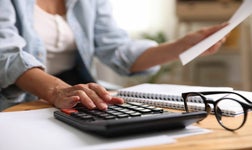 Budget planning. Woman using calculator while working with accounting document at table indoors, closeup