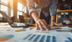 A person looks at profit and loss data on sheets of paper on a table.