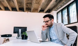 Business man sitting at desk and looking pensively at laptop.