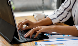 woman using laptop surrounded by graphs and other accountancy software images on printed paper sitting on desk
