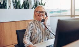 Smiling business woman sitting in front of desktop answering phone