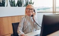 Smiling business woman sitting in front of desktop answering phone