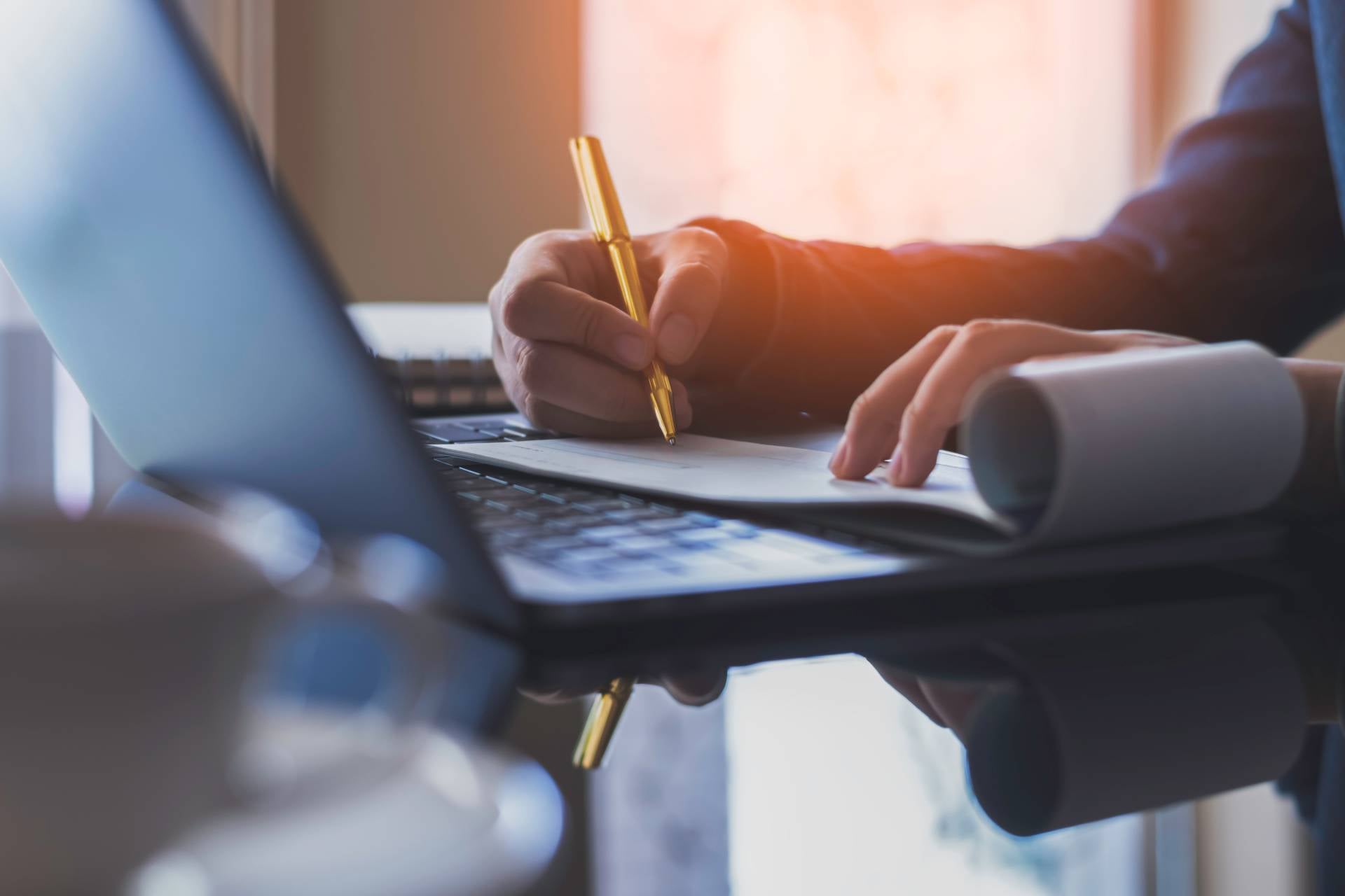 Business woman hand write and sign cheque book with laptop computer on the desk at office. Check payment, paycheck and payroll conceptual