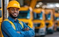 A confident worker smiles while standing in front of a fleet of yellow trucks in a warehouse. He showcases the importance of teamwork and dedication in the logistics industry.