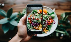 Hands holding smartphone capturing appetizing dishes with professional photography