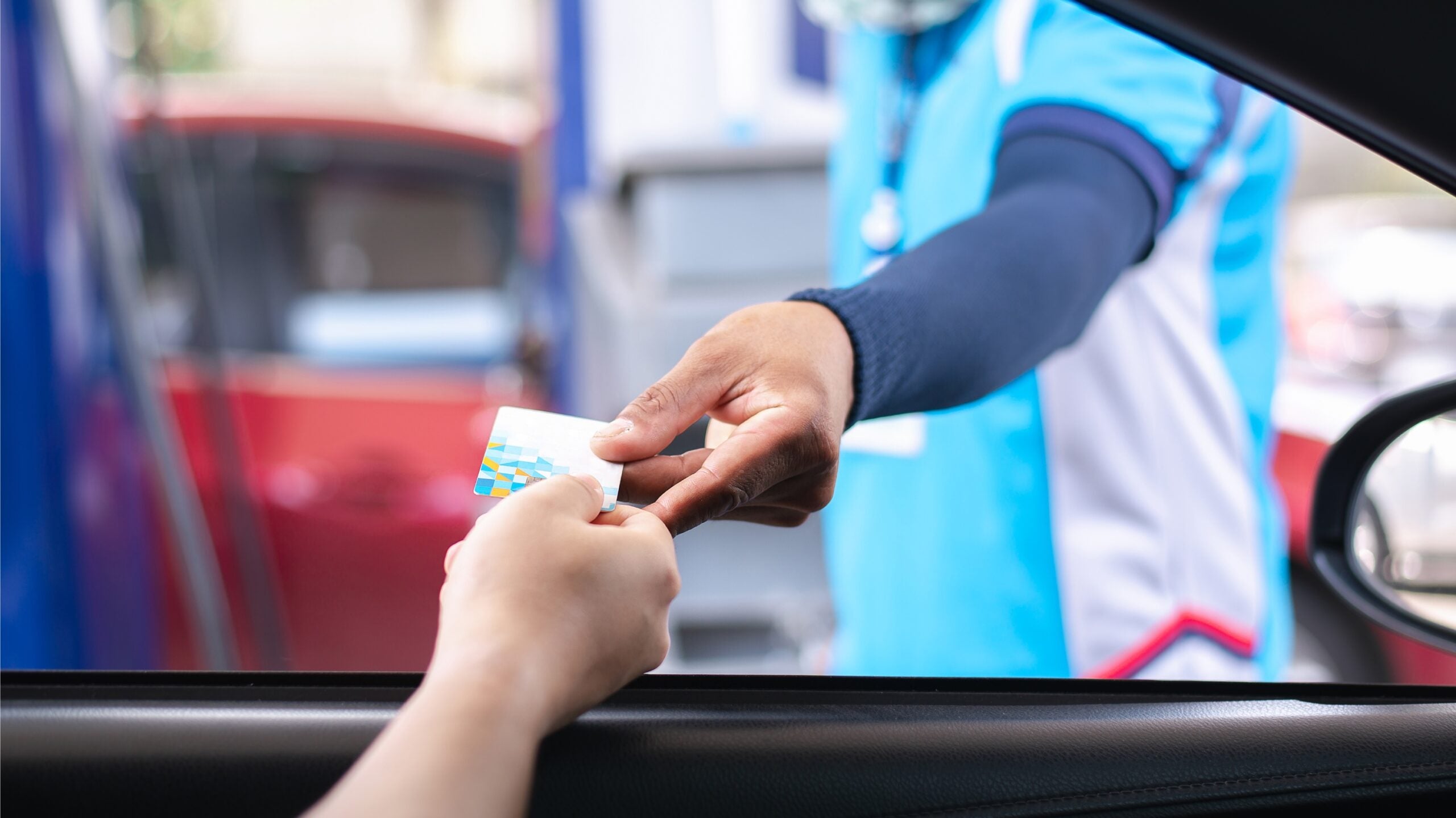 hand coming out of vehicle window to pass fuel card to pump operator to pay at gas station